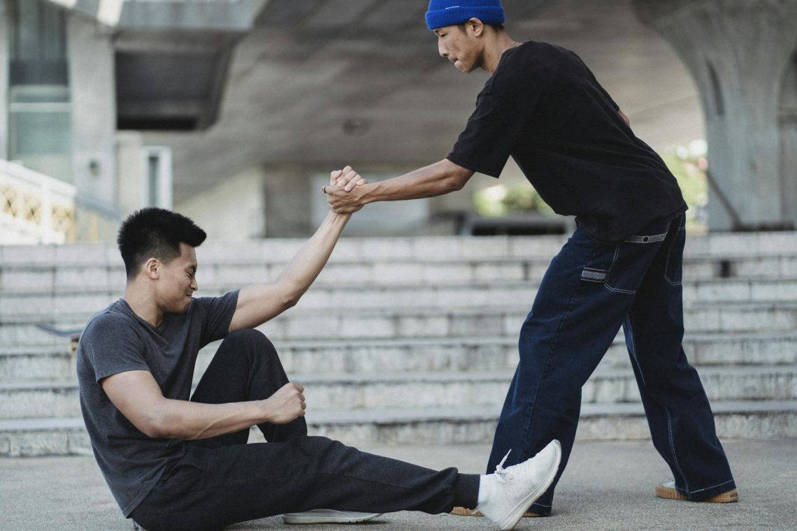Asian man helping friend to get up from ground. offering a helping hand.